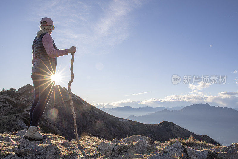 女性徒步旅行者与徒步手杖手表日落在山上