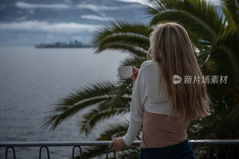 一个年轻女子在她的阳台上喝着茶，可以看到湖景
