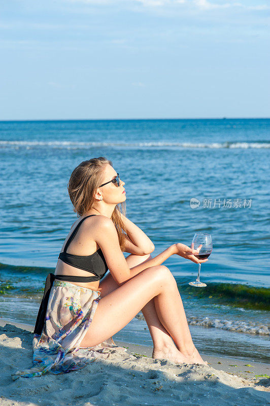 年轻女子坐在海滩上，手里拿着酒杯