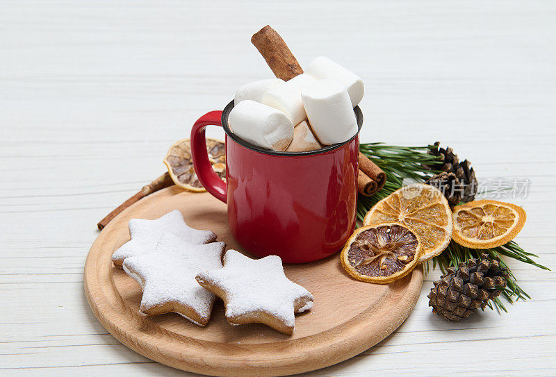 红色的杯子和热巧克力可可饮料装饰棉花糖和肉桂棒在木板上的生姜饼干洒糖粉和干橙片，松果和树枝