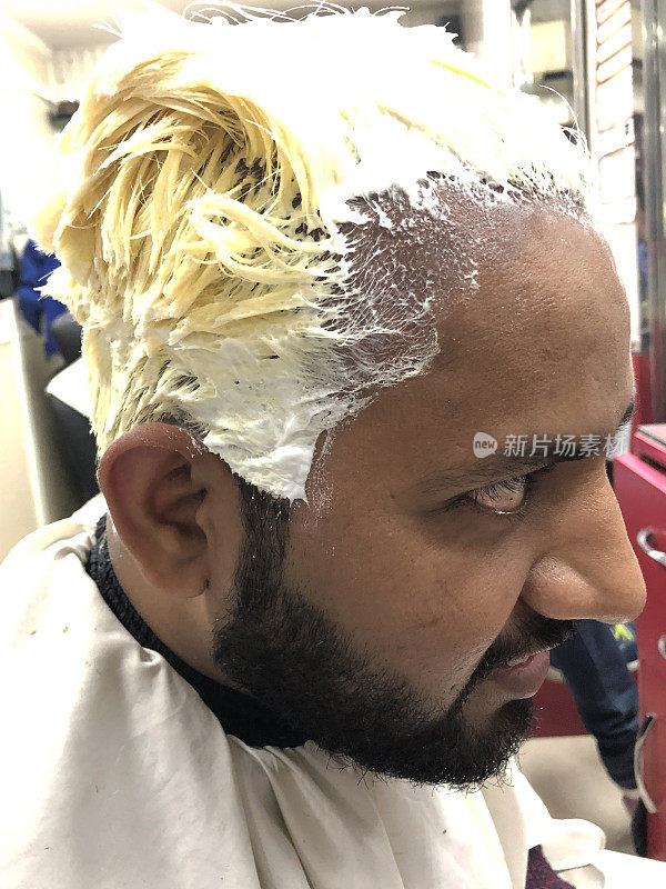 美发沙龙里一个印度男人的特写照片，黑色的头发被化学物质漂白成金色，大头照，侧面图