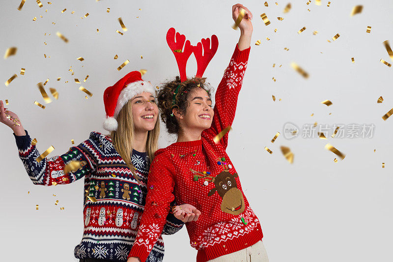 圣诞节到了!两个美丽的女人穿着圣诞毛衣，周围撒着五彩纸屑