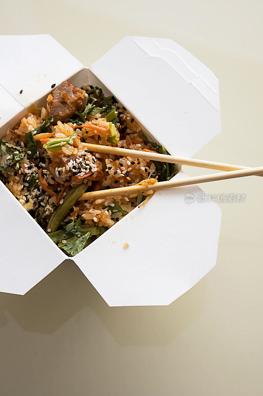 外卖盒里的米饭，猪肉和蔬菜，桌子上有筷子。外卖的美味中式炒锅。