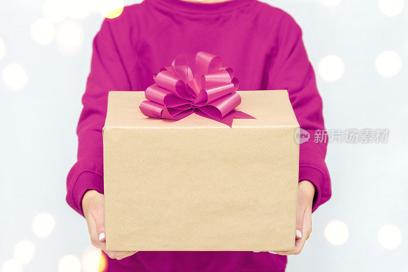 女人手中的礼物。快递。一名身穿紫色运动衫的年轻女子拿着一个带蝴蝶结的纸箱。