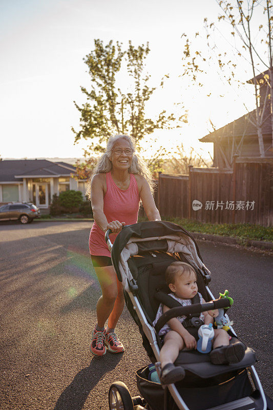 慈爱的奶奶推着婴儿车里的小孙女在附近散步