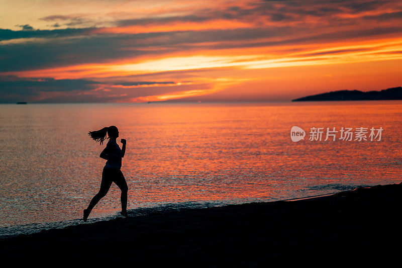 一个女人的剪影，扎着马尾辫，在海边奔跑，享受着美丽的日落和天空。