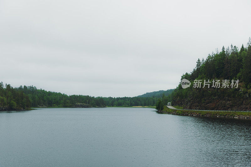 露营车行驶在公路上，可以看到瑞典的湖泊和森林的壮观景色