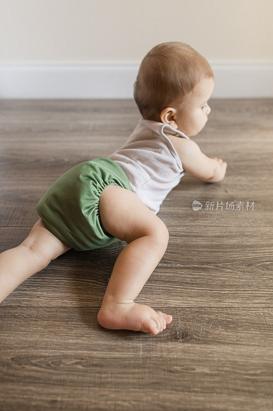 2022年，患有多指畸形的7个月大的大流行男婴，穿着橄榄绿颜色的可重复使用和可持续的布尿布，在家里的木地板上爬行，以下犬式和腹部躺着
