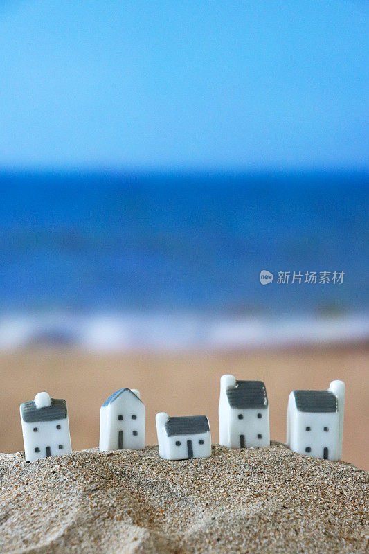 沙滩上的一排模型度假别墅的特写图像，沙滩背景与海浪在退潮时破碎，大海和海岸线，度假租赁和度假屋概念，重点在前景