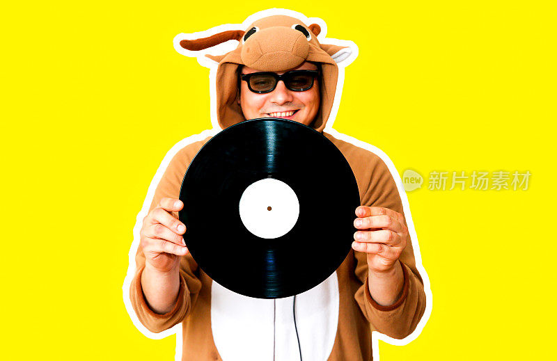一个人穿着奶牛的角色扮演服装，在黄色背景上放着留声机唱片。穿动物睡衣的人。派对创意的搞笑照片。迪斯科复古音乐。