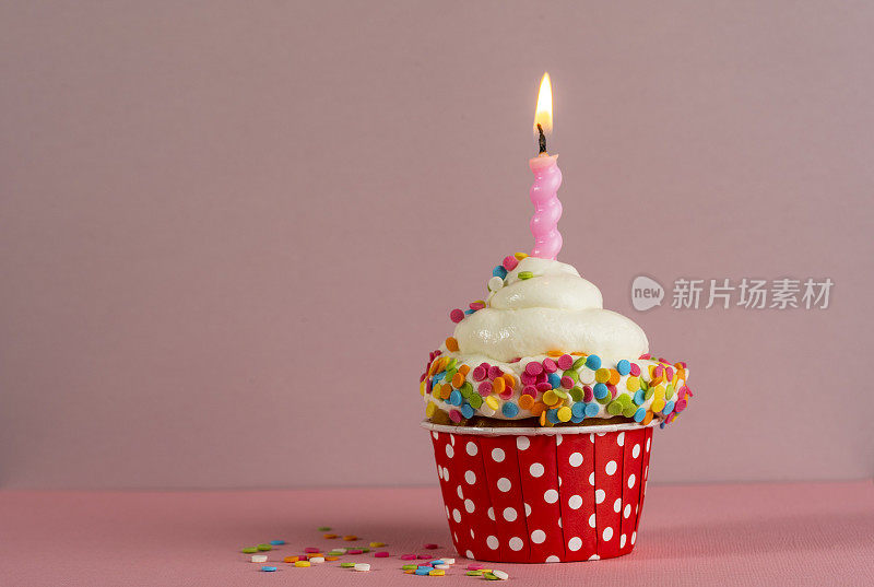 生日小蛋糕，粉色背景上有烛光。白色奶油蛋糕和糖果装饰。节日甜点，恭喜你。生日快乐。