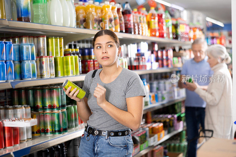 一名年轻女子在超市的食品杂货区挑选装在铝罐里的碳酸饮料