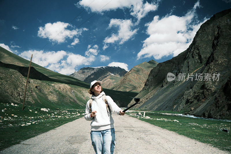 开朗的成熟女性背包客在天山的高地路上拍摄视频