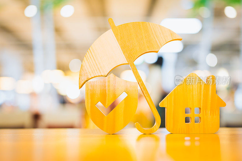 模型的伞和盾保护图标与房屋在木桌上的保险制度的概念储蓄和住房保险的迫在眉睫的损失和火灾，建筑火灾保险的概念。