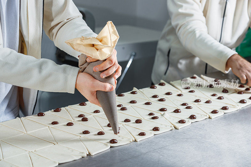 用裱花袋把巧克力奶油挤在三角形面团上