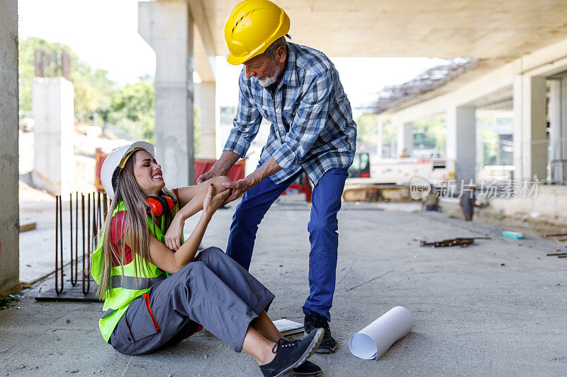 年轻的女建筑工人在建筑工地受伤，她的资深同事正在帮助她。