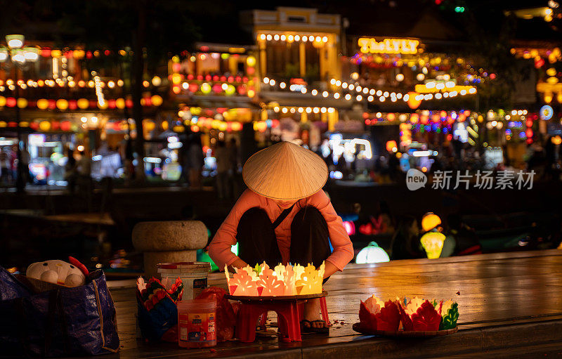 年轻的越南妇女在会安夜市出售传统的蜡烛和灯笼。