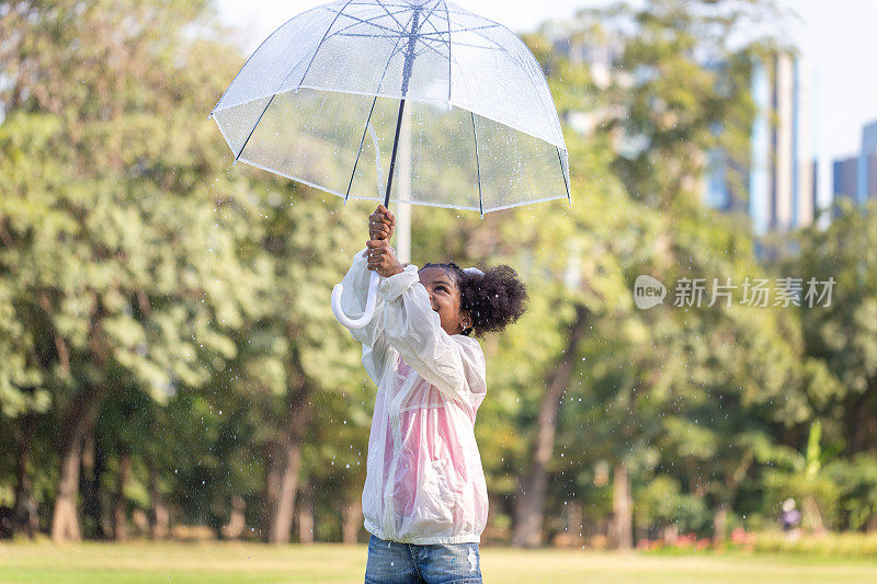 小女孩撑着伞在公园里玩雨，小女孩在户外的花园里玩