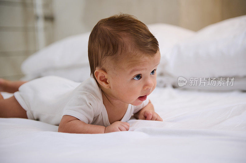 可爱的4个月大的男婴在白色的阳光卧室。在俯卧时间，新生儿在床上放松。复制广告位