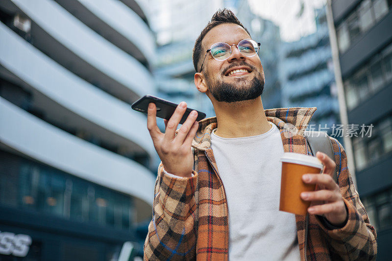 年轻的成年男子边走边打电话边喝外卖咖啡。