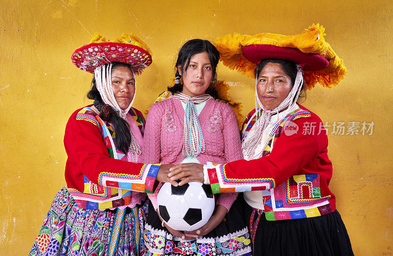 黄色背景的肖像，三个微笑的女孩足球运动员，来自克丘亚族，手里拿着球。克丘亚妇女没有任何方式传递团队和同志情谊