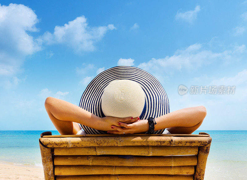戴着帽子的女人在海滩上放松，看着大海。副本的空间。