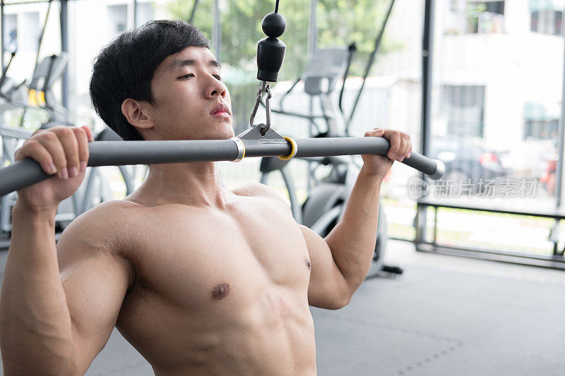年轻人在健身中心用举重机锻炼。男运动员在健身房用下拉机锻炼肌肉。运动健将在健身俱乐部锻炼。