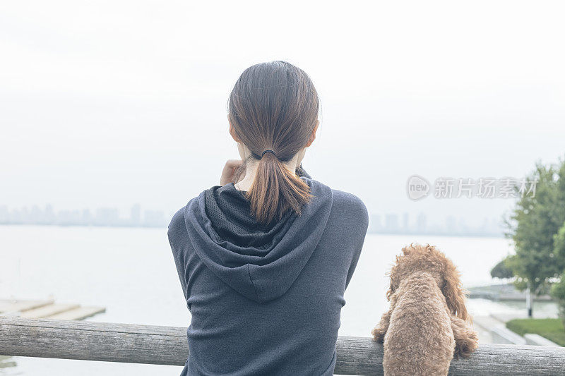 后视图的女人和可爱的小狗靠在栏杆上看风景