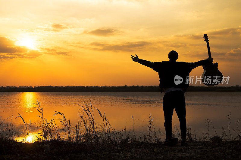 夕阳下，挎着吉他的男人的剪影