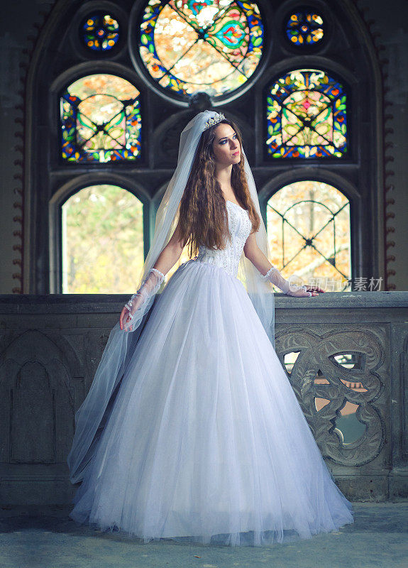 年轻的新娘穿着婚纱站在教堂的阳台上