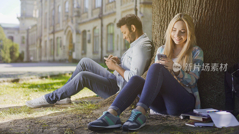年轻人坐在树下，使用手机，对自己微笑，快乐