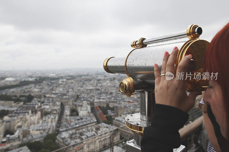 一个年轻的成年女子在埃菲尔铁塔上用望远镜看