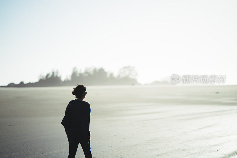 一个年轻女子的剪影是散步在一个雾蒙蒙的海滩在日落