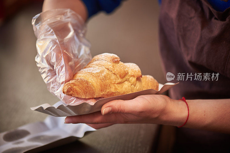 女咖啡师在咖啡店的顾客面前提供新鲜的羊角面包