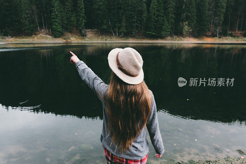 戴着帽子的女人在山湖边给你指路