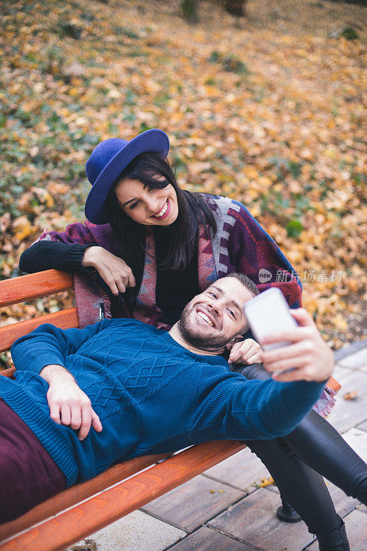 一对可爱的情侣在秋天的公园长椅上自拍