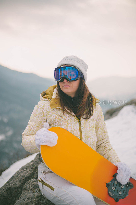 女人拿着滑雪板，背景是高山