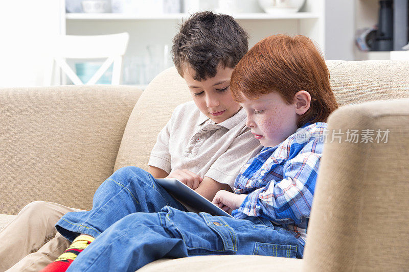 两个男孩坐在沙发上用电子平板电脑在家