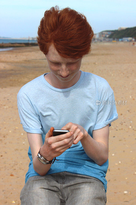 海边，一个男孩在用手机发短信