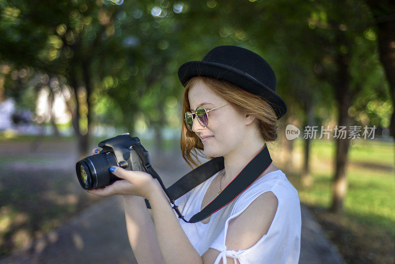 微笑的年轻女子肖像与数码相机对着树木区域
