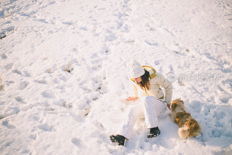 一个女人带着狗在雪地里走在村里的街道上