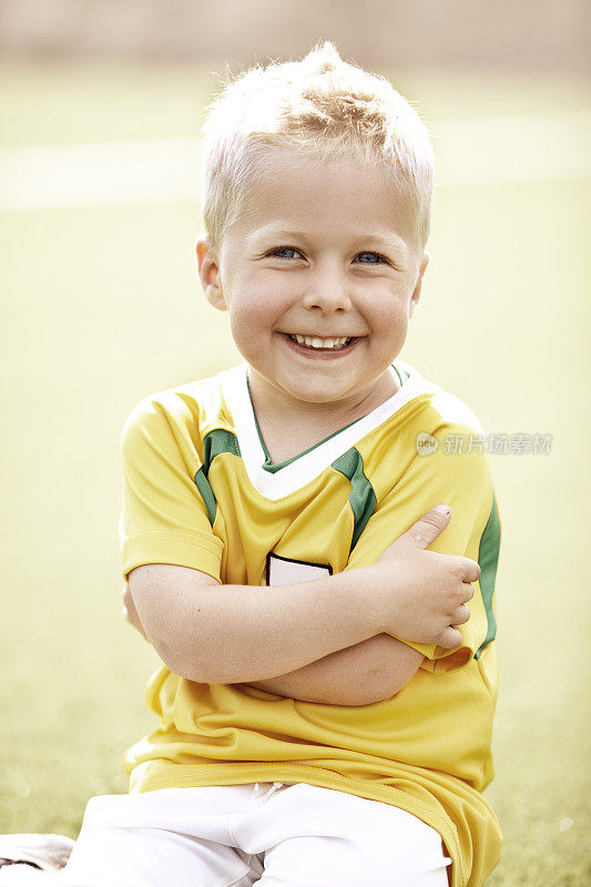 一个四岁的男孩坐在足球场上