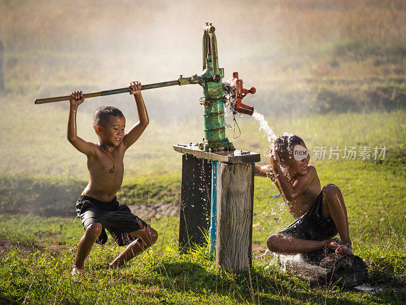 两个小男孩摇晃地下水洗澡，泰国乡村。