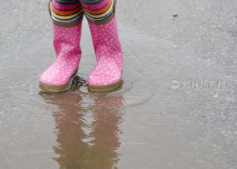 小女孩穿着雨靴在水坑里戏水