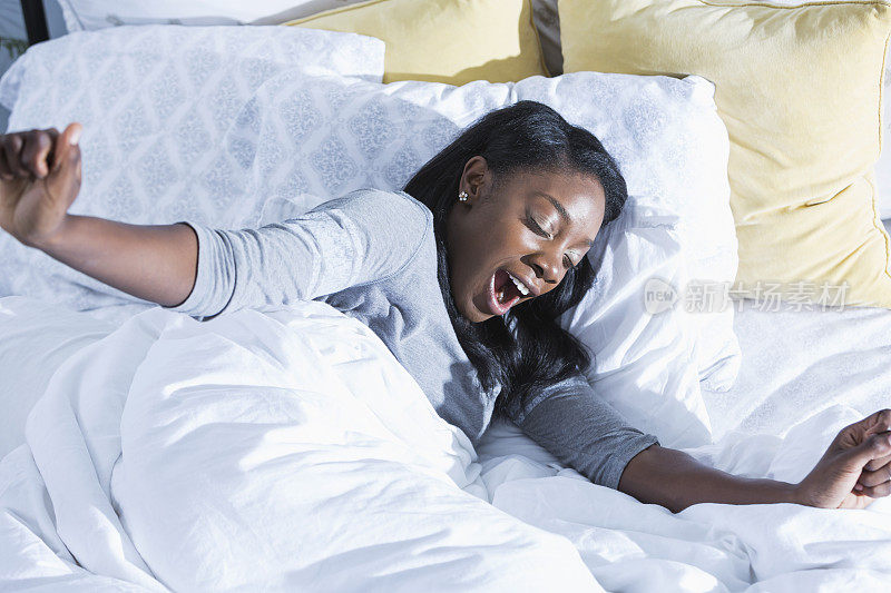 一位年轻的非洲裔美国妇女躺在床上，打着哈欠