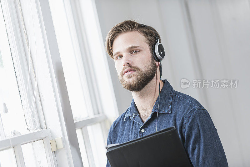 一个戴着耳机的年轻人站在窗边