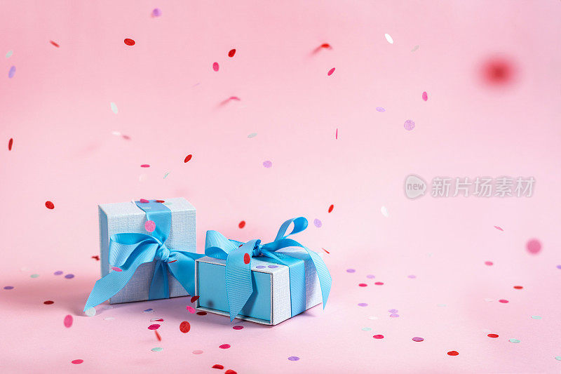 派对时间概念!两个漂亮的蓝色包装的礼物或礼品盒与丝带隔离在明亮的粉红色背景与复制或空白的文字与纸和彩色的五彩纸屑装饰