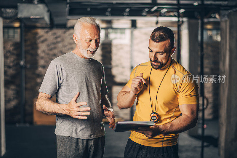 活跃的老年人在一个健身房的交叉训练区和他的私人教练跑步通过锻炼表