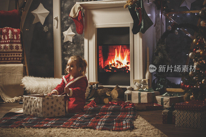 快乐的小女孩在壁炉边打开她的圣诞女孩