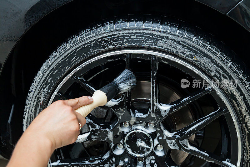 一名男性工人在汽车修理厂用一种特殊的铸轮刷清洗一辆黑色汽车，并将表面擦得发亮。汽车服务行业。